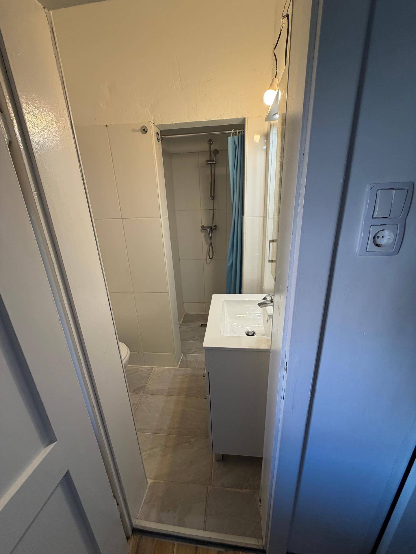 Schmales Badezimmer mit Waschbecken und einer Duschkabine, gefliestem Boden und Wänden.