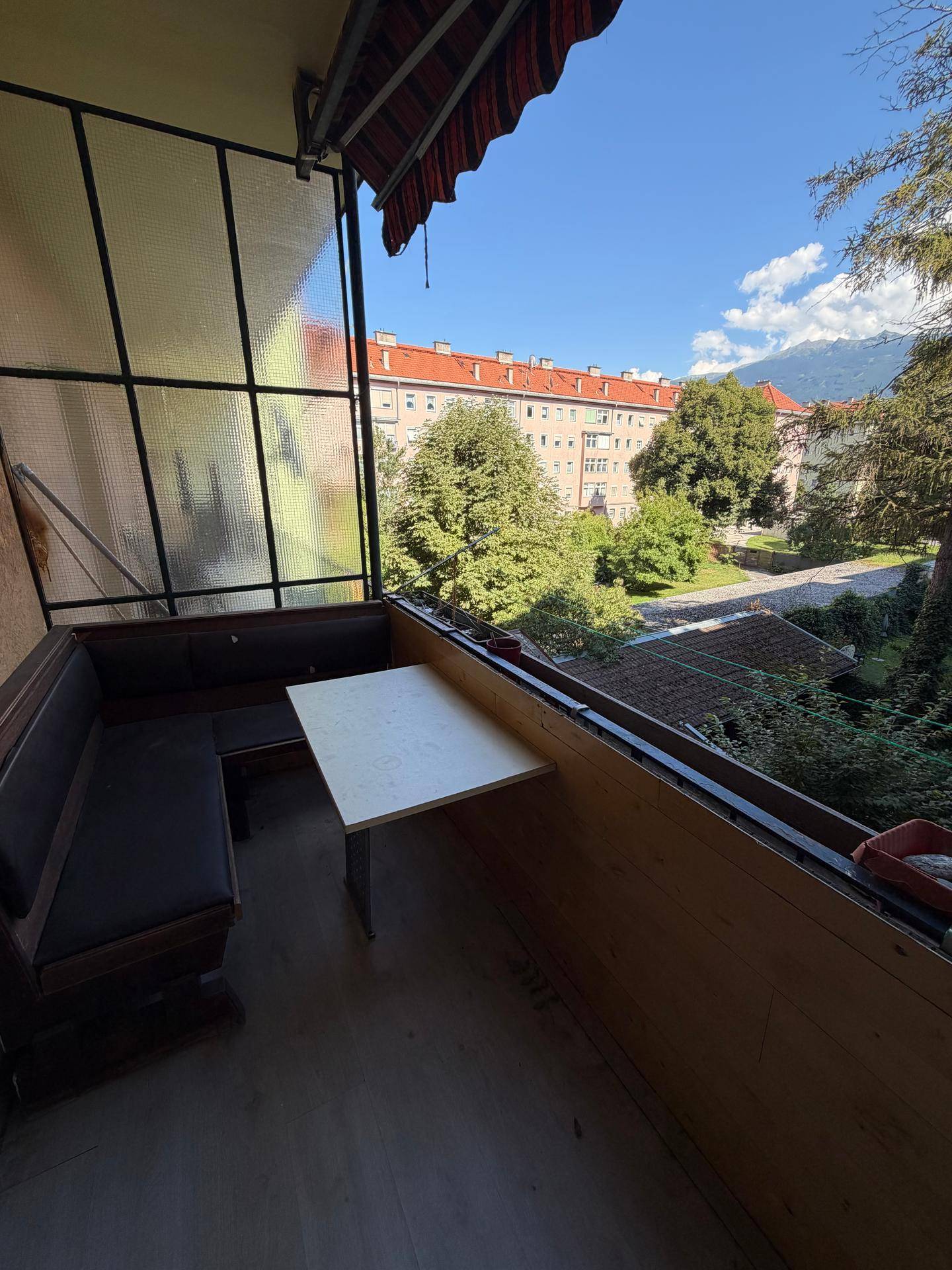 Sonniger Balkon mit Sitzgelegenheiten und Blick auf grüne Bäume und umliegende Gebäude.