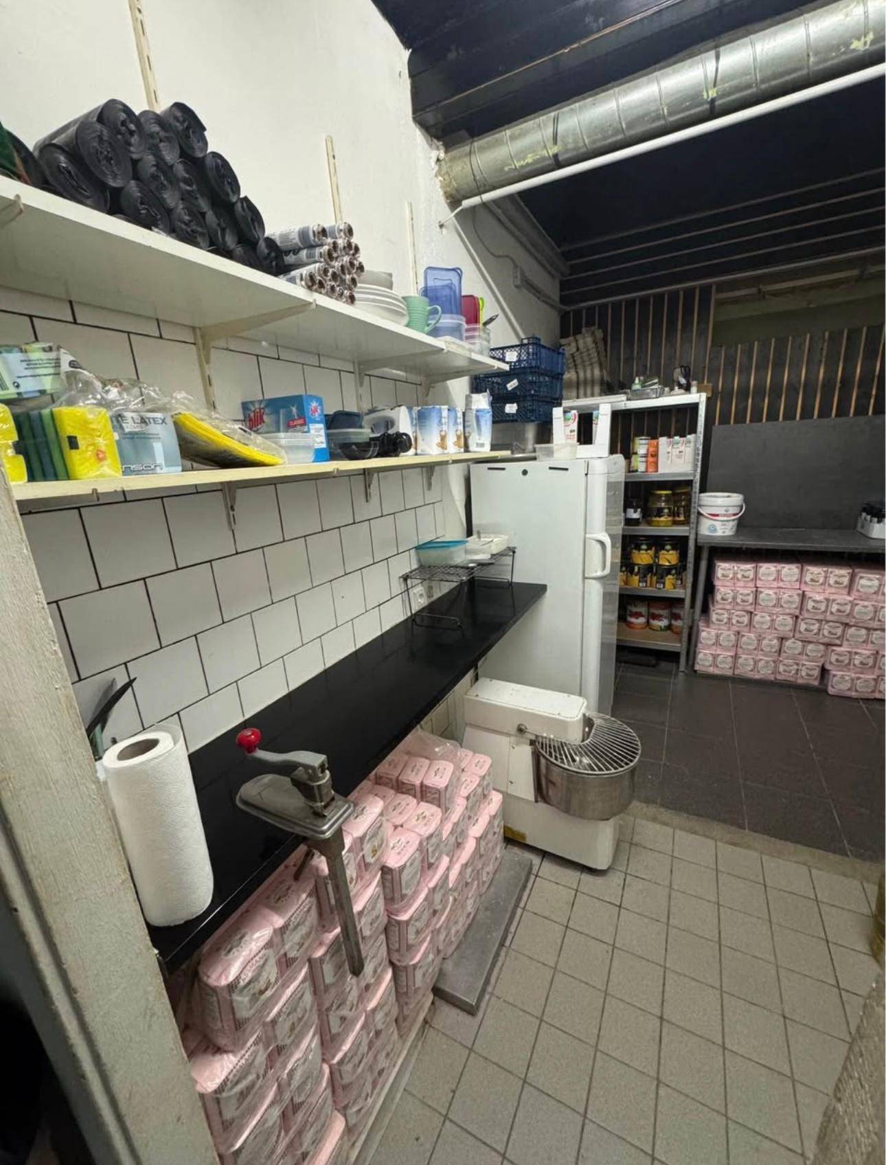 Hinterküche oder Vorbereitungsbereich mit Regalen, Fliesenwänden und einem Kühlschrank.