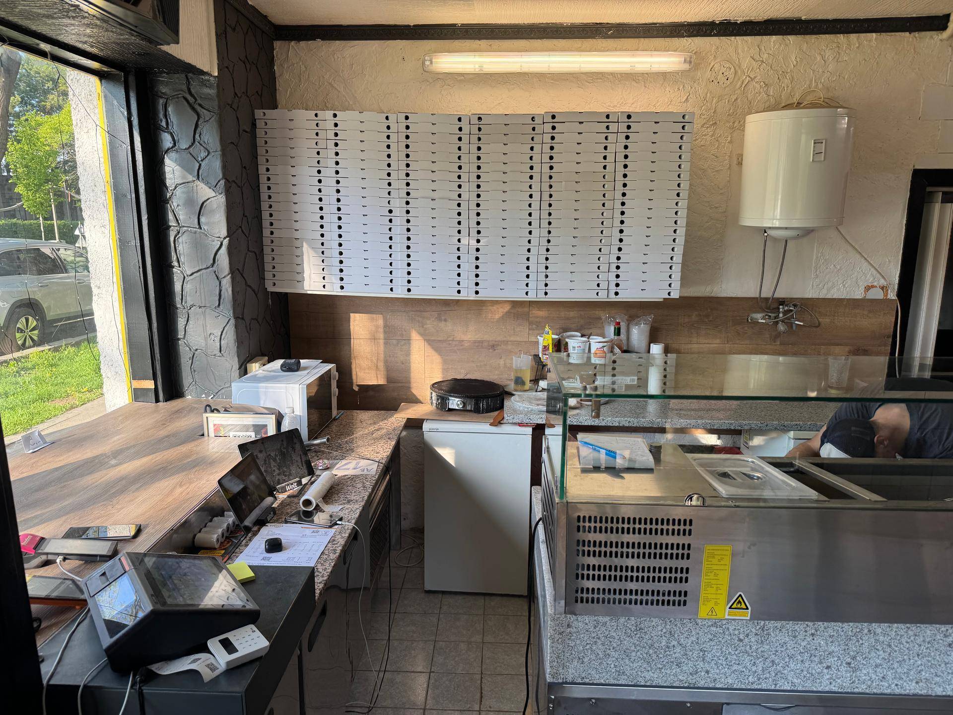 Hauptküchenbereich eines Imbisses mit Theke, Pizza-Kartons und verschiedenen Küchengeräten.