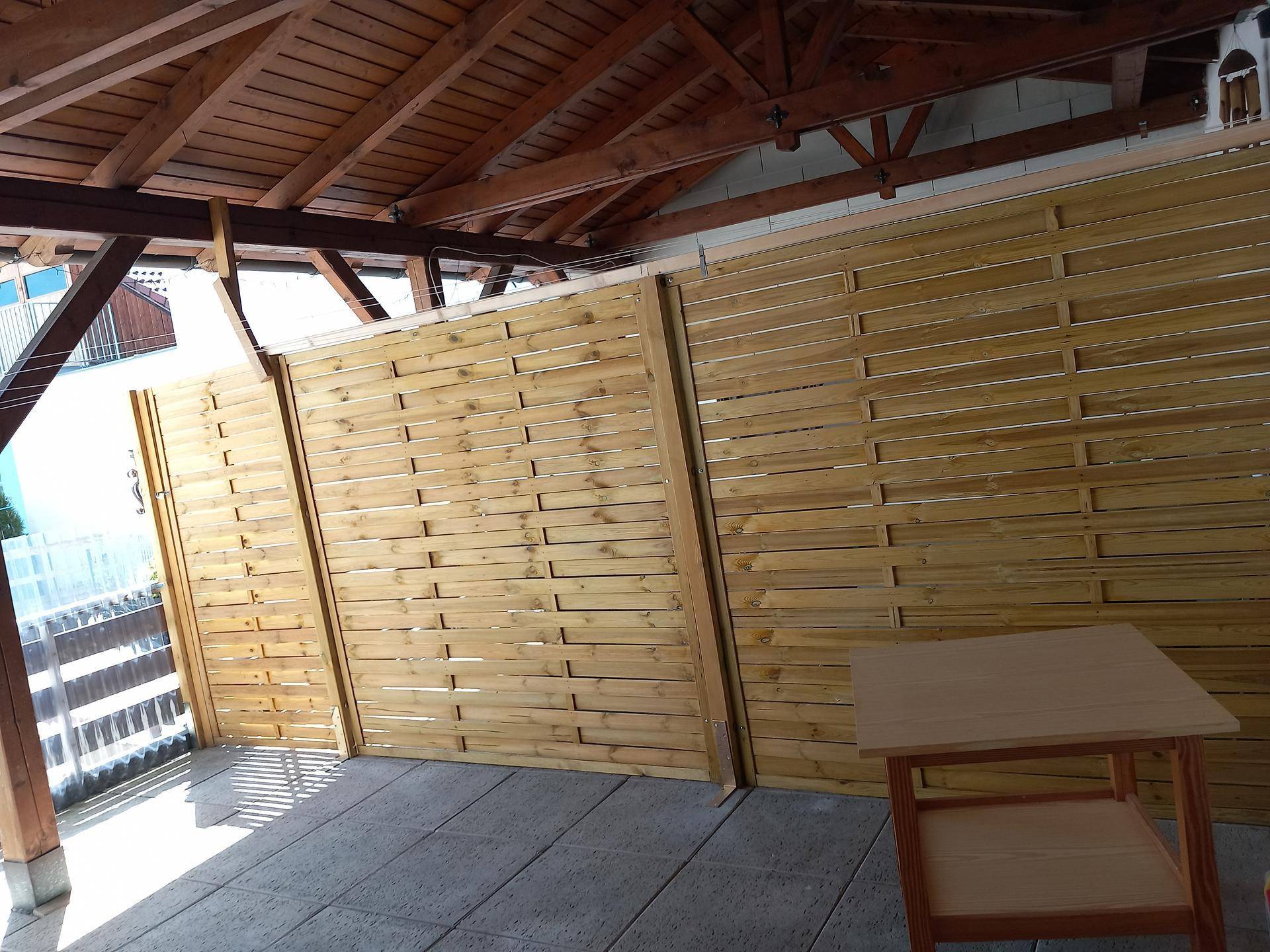 Überdachte Terrasse mit Holzdachkonstruktion, Sichtschutzwänden und gefliestem Boden.
