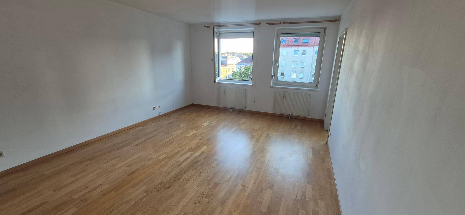 Geräumiges, helles Zimmer mit Parkettboden und zwei Fenstern, die viel Tageslicht hereinlassen.