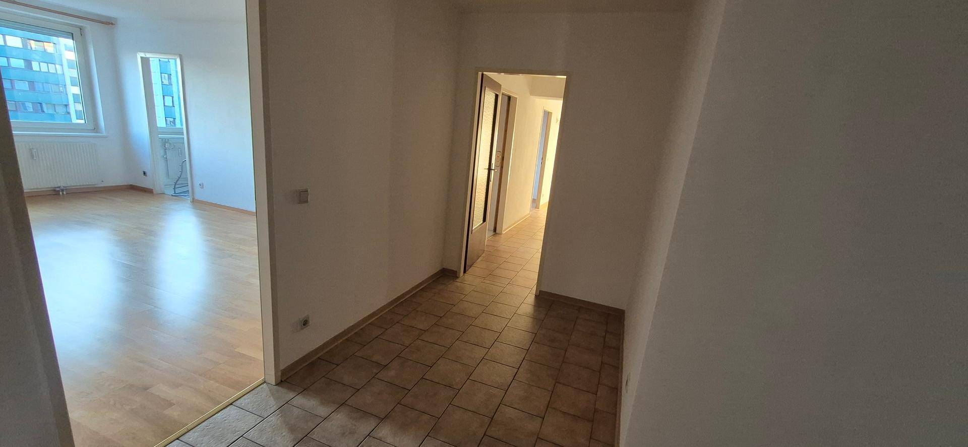 Flur mit Fliesenboden, der zu einem hellen Zimmer mit Holzfußboden führt.