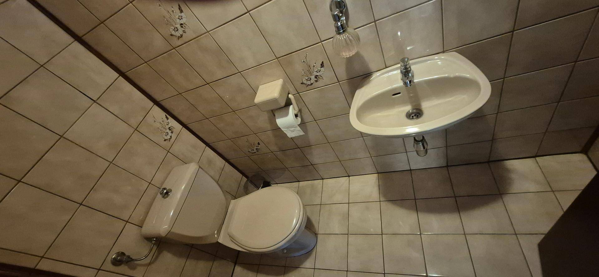 Kleines WC mit Fliesen an Wänden und Boden, ausgestattet mit Toilette und Waschbecken.