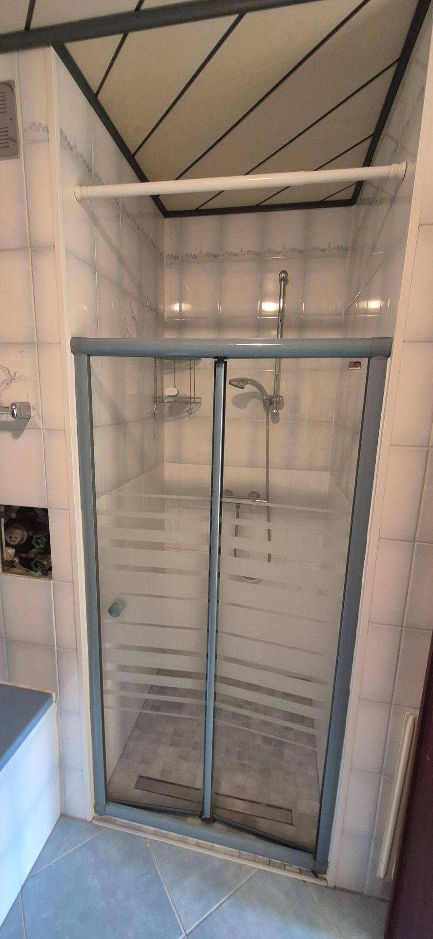 Duschkabine mit Glastüren in einem gefliesten Badezimmer mit Holzdeckenverkleidung.