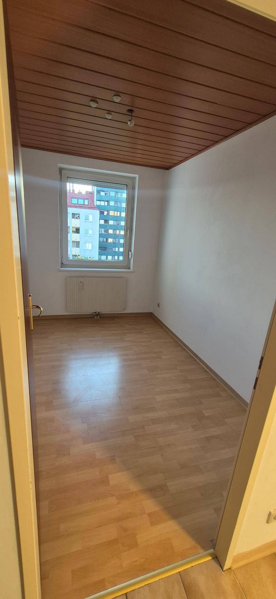 Helles Zimmer mit Laminatboden, Holzdecke und einem Fenster mit Blick auf die Umgebung.