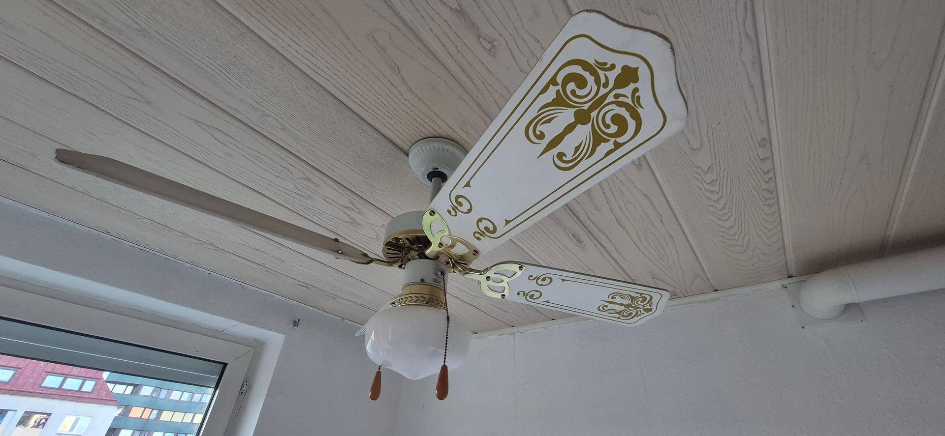 Deckenventilator mit dekorativen Elementen an einer Holzdeckenverkleidung.