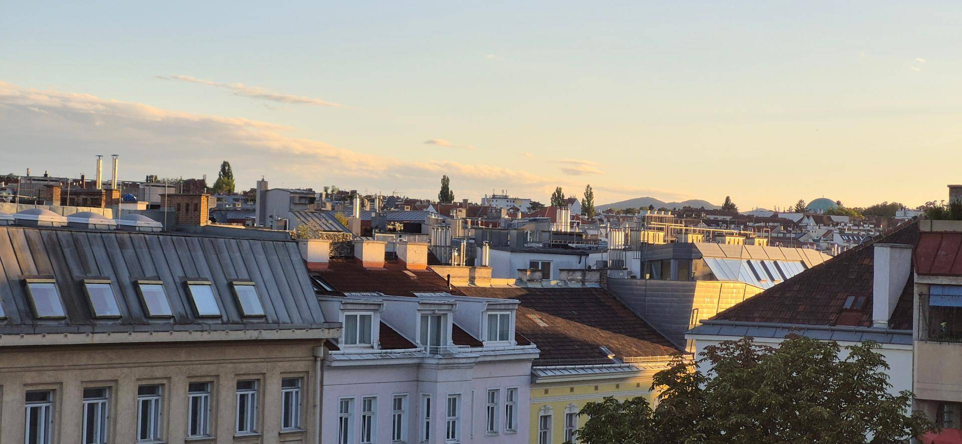Panoramablick über die Dächer einer Stadt bei Sonnenuntergang mit Bergen im Hintergrund.