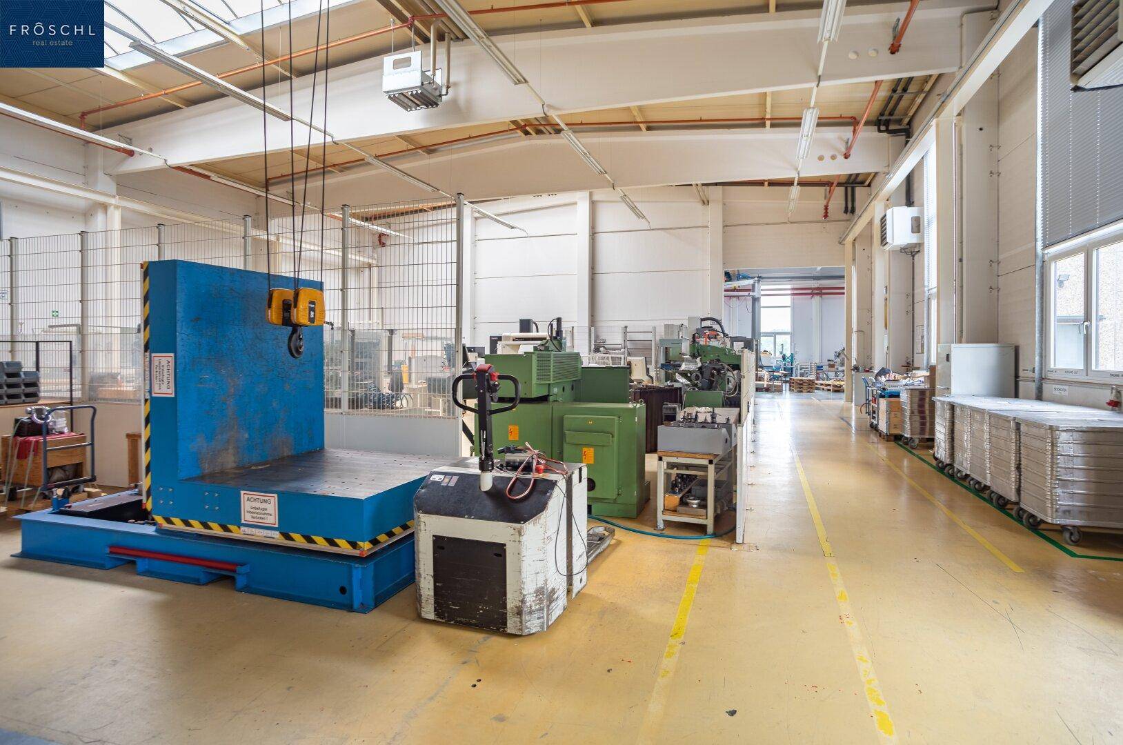 Weitläufige Industriehalle mit großen Maschinen, gelben Bodenmarkierungen und Oberlichtern für viel Tageslicht.