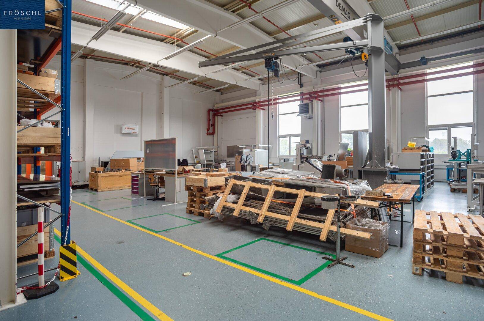 Lager- und Montagebereich mit Regalen, Paletten und großen Fenstern, die viel Tageslicht hereinlassen.