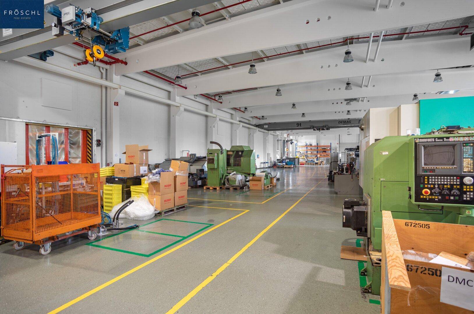 Produktionsbereich mit verschiedenen Maschinen, Lagerboxen und einem Kranbahnsystem an der Decke der Halle.