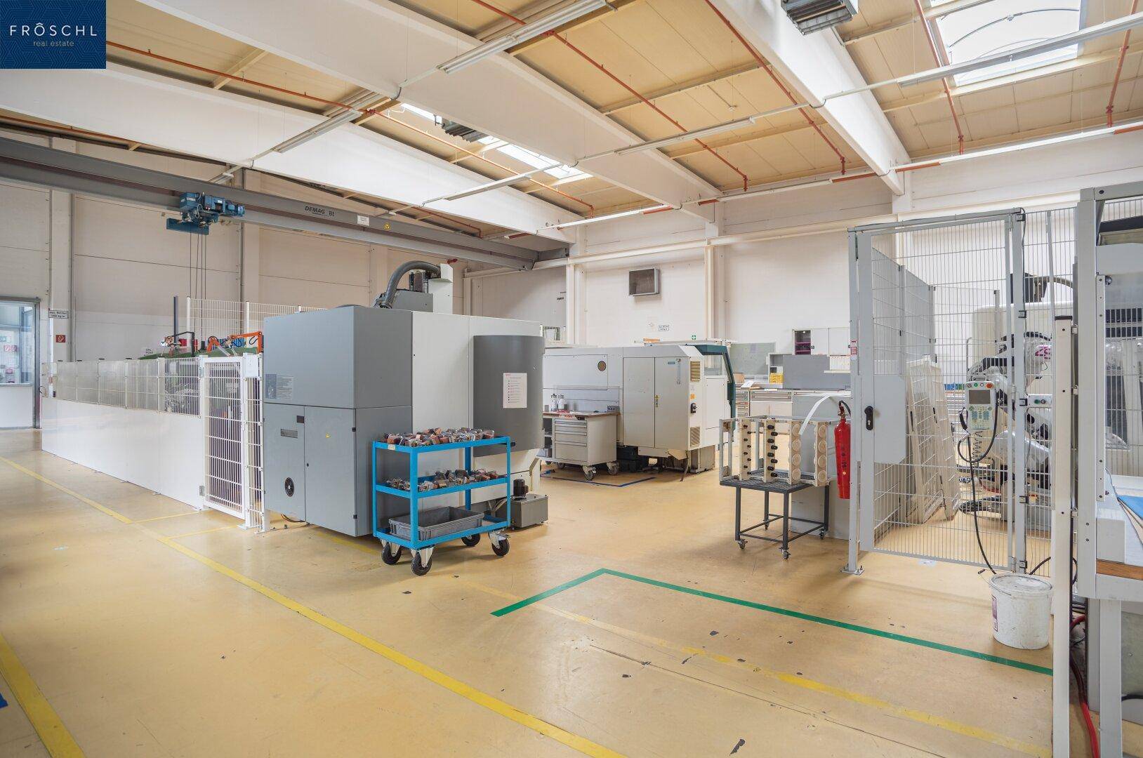 Großzügige Produktionshalle mit verschiedenen Maschinen, hohen Decken und Oberlichtern für Tageslicht.