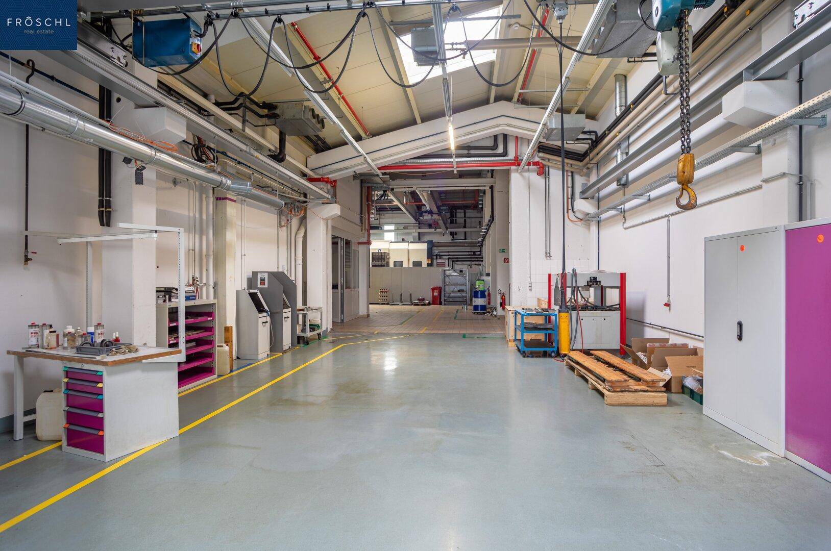 Industrieller Gangbereich mit sichtbaren Rohrleitungen, Lüftungskanälen und hohen Decken in der Halle.