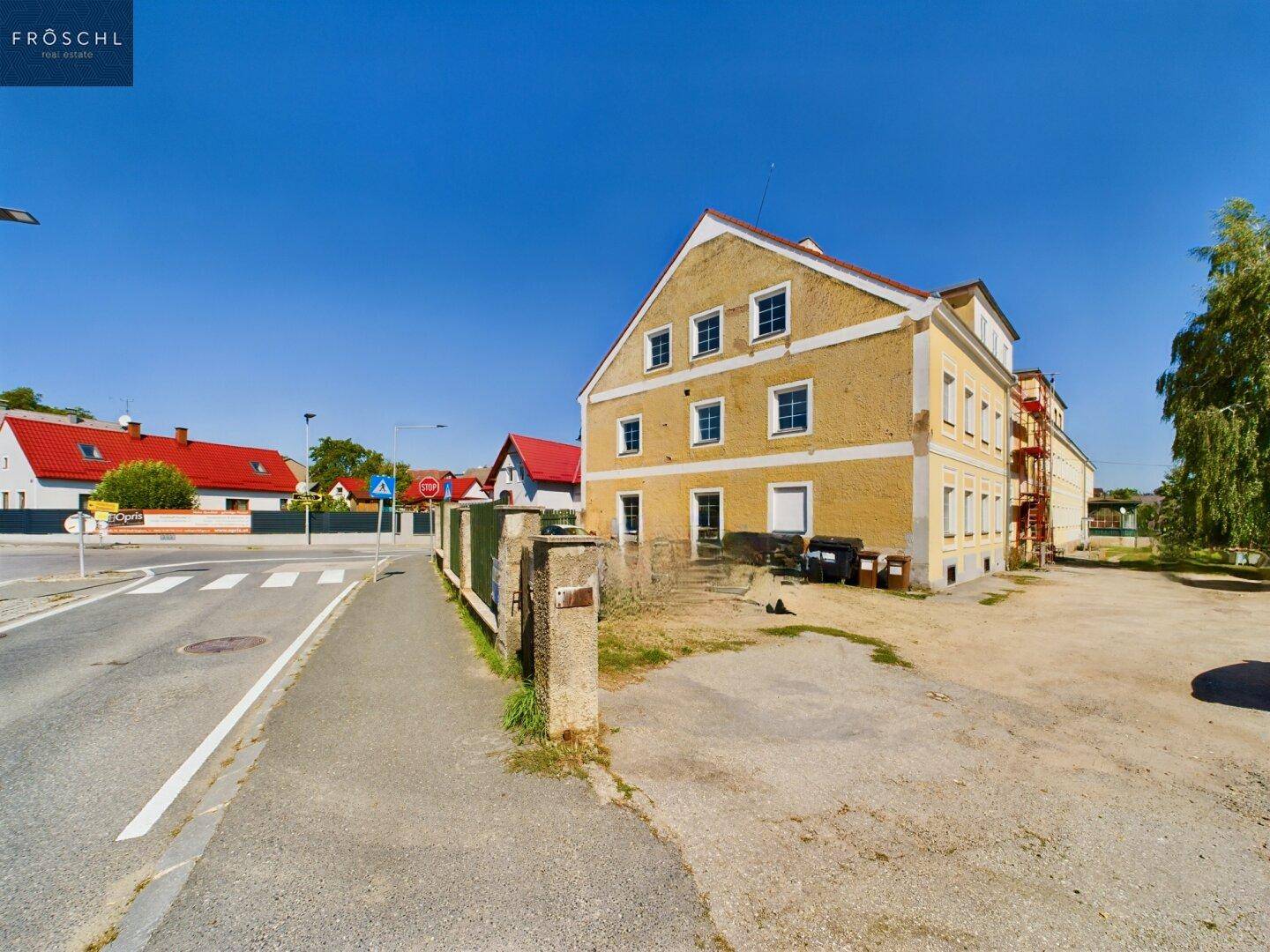 Historisches Gebäude mit gelber Fassade und mehreren Fenstern an einer ländlichen Straße.