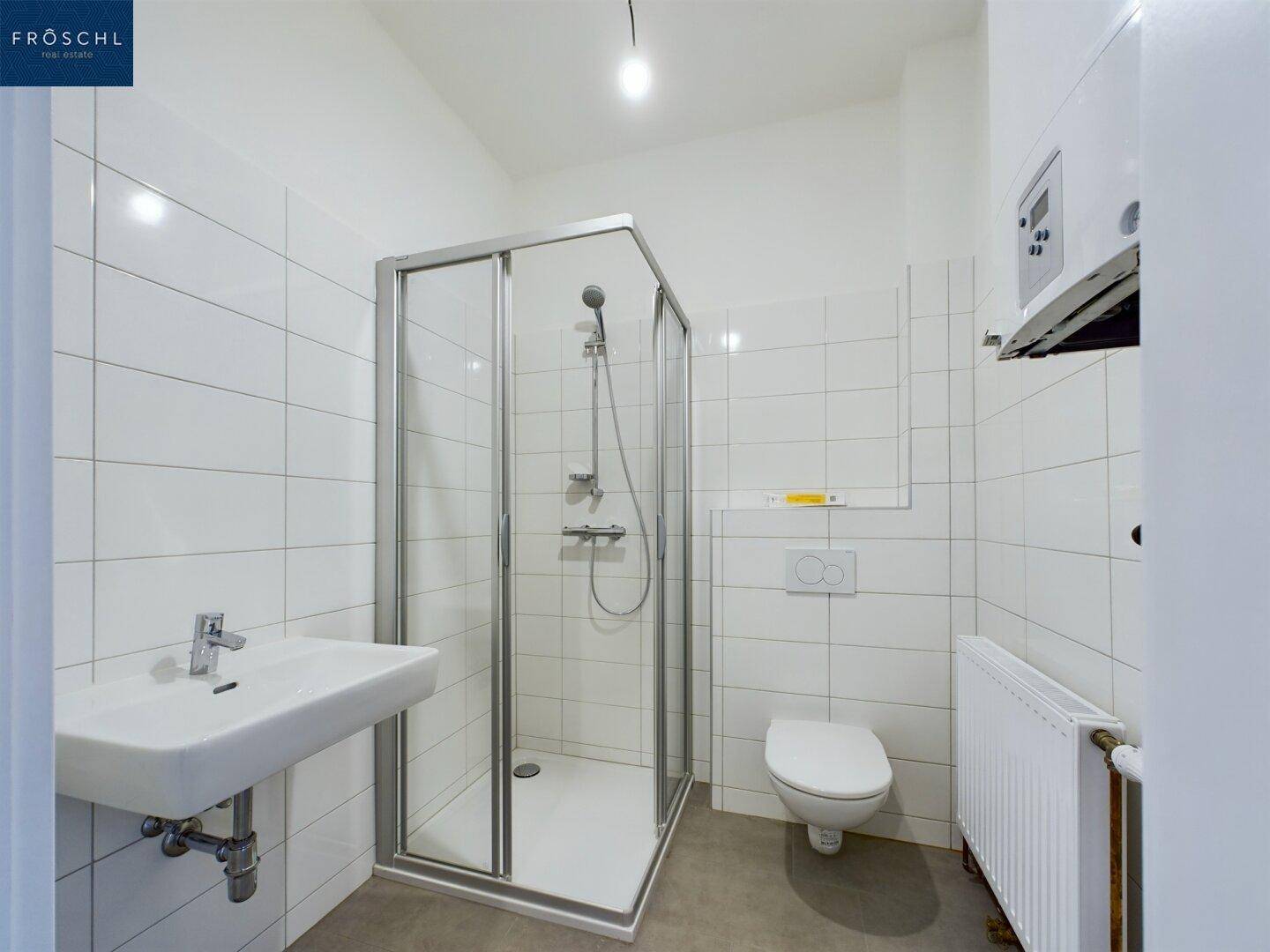 Modernes Badezimmer mit weißen Fliesen, Duschkabine, WC und Waschbecken.