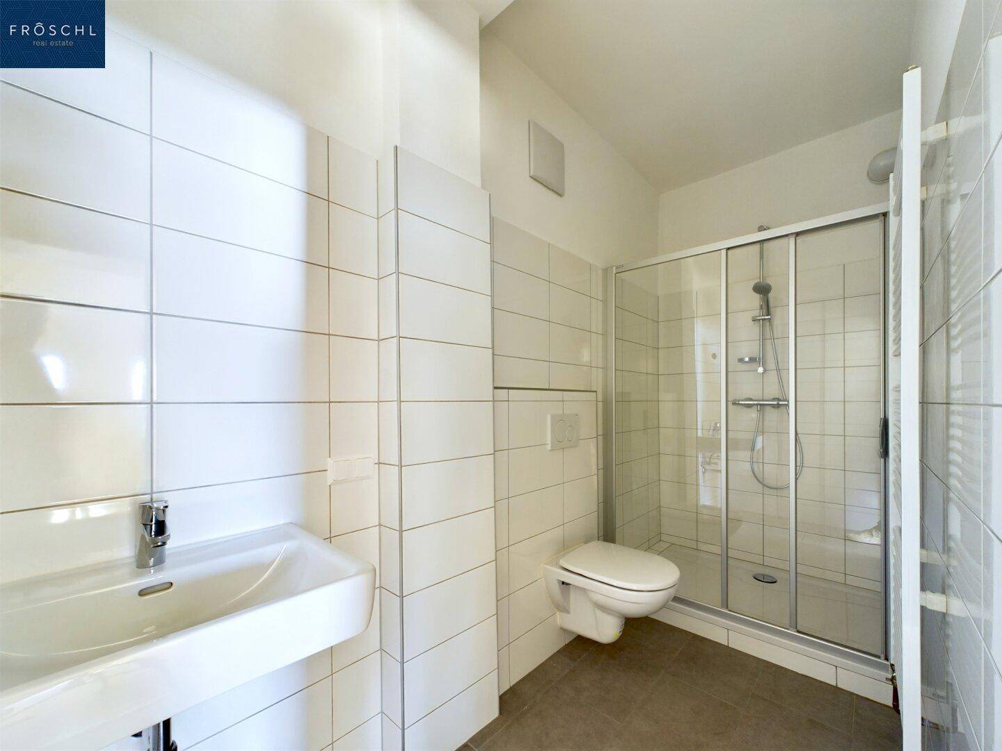Modernes Badezimmer mit weißen Fliesen, Duschkabine, WC und Waschbecken.