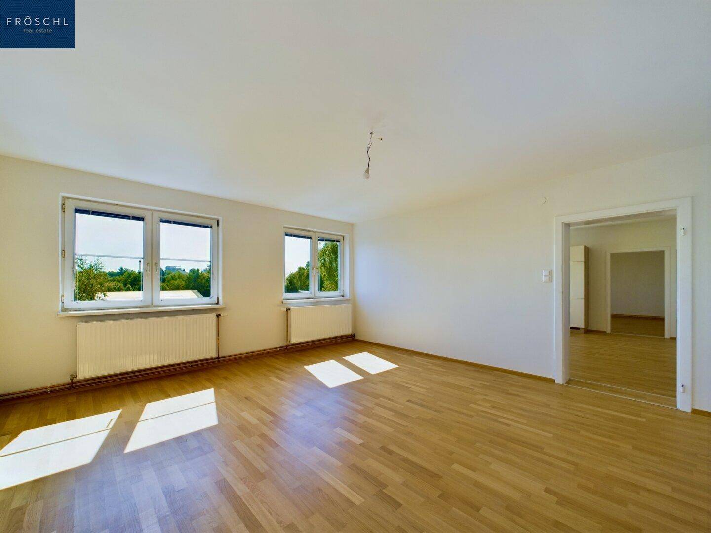 Heller Wohnraum mit Holzboden, zwei Fenstern und viel natürlichem Licht.