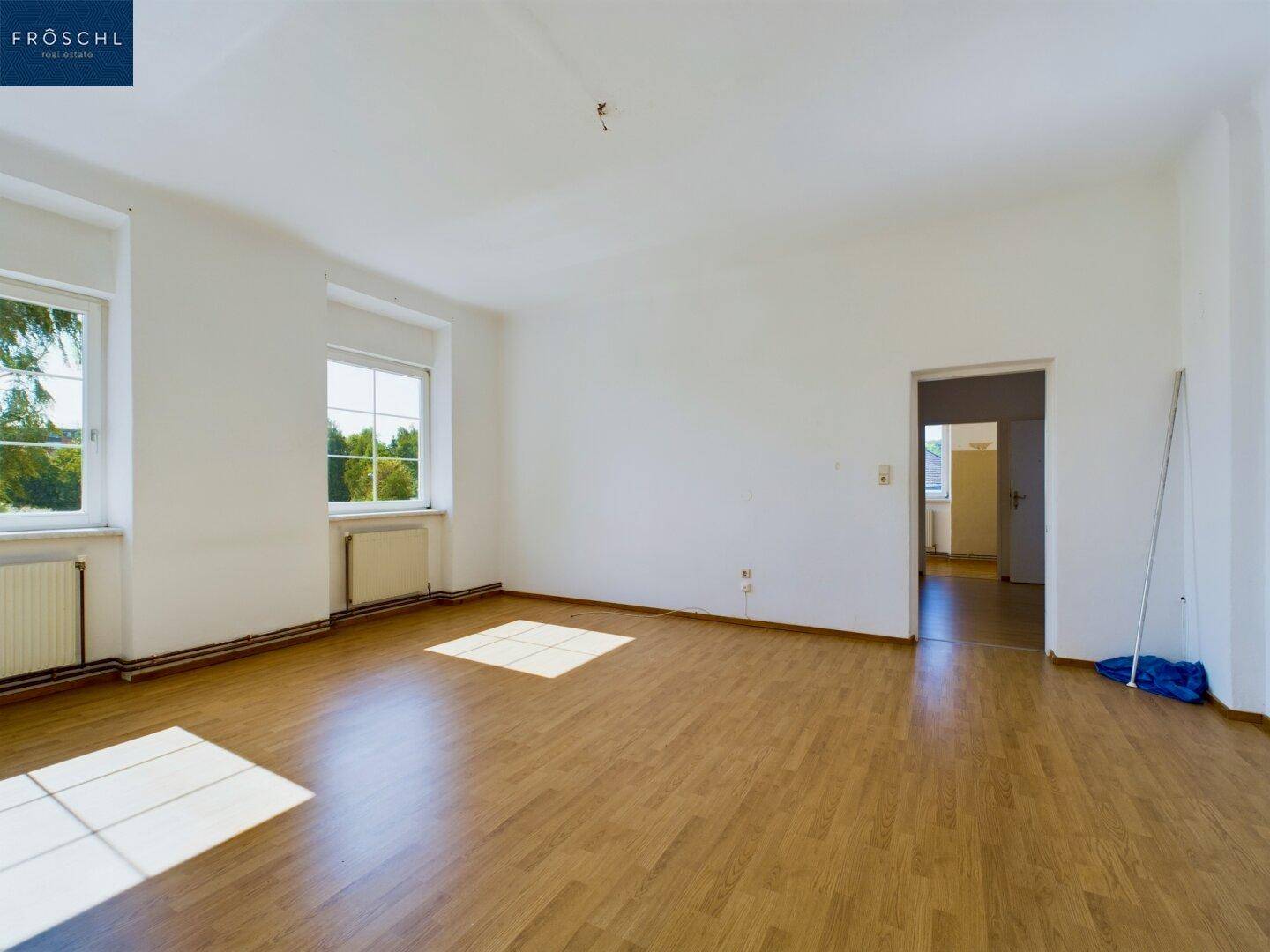 Heller Wohnraum mit Holzboden, zwei Fenstern und viel natürlichem Licht.