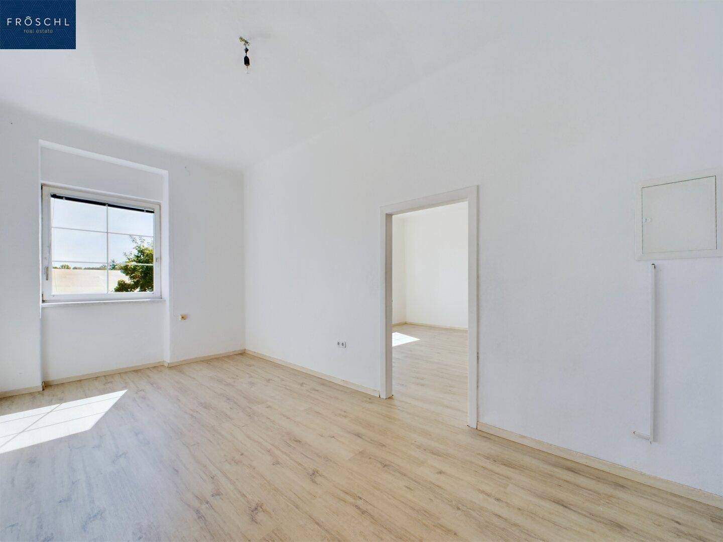 Heller Raum mit Laminatboden und einem Fenster, das viel natürliches Licht hereinlässt.