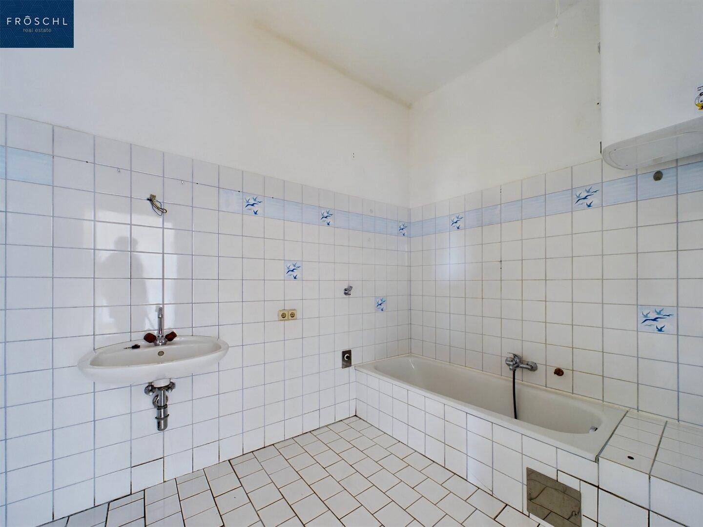 Badezimmer mit Badewanne, Waschbecken und weißen Fliesen mit blauen Akzenten.