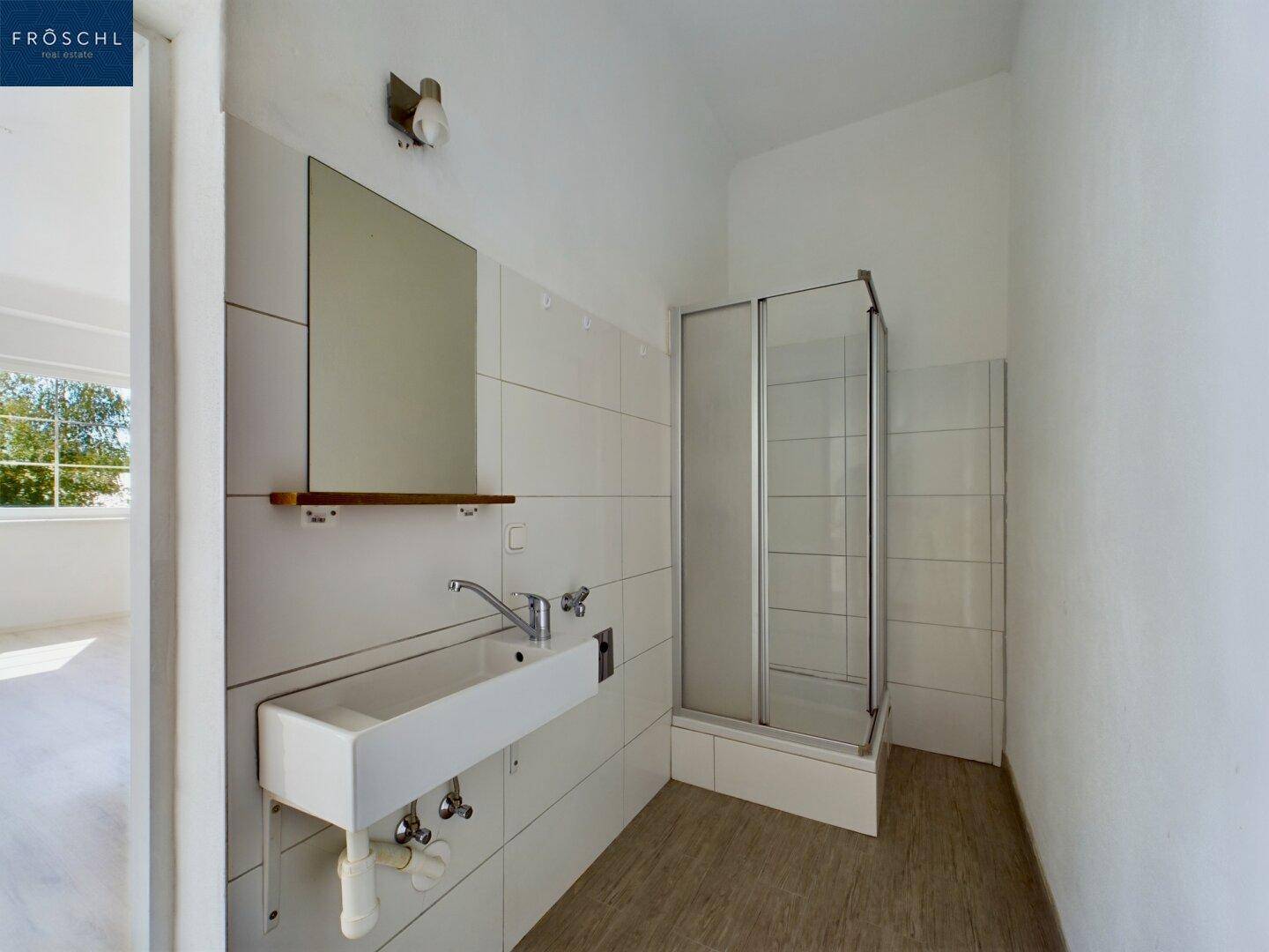 Helles Badezimmer mit Duschkabine, Waschbecken und Spiegel, bereit für die individuelle Gestaltung.