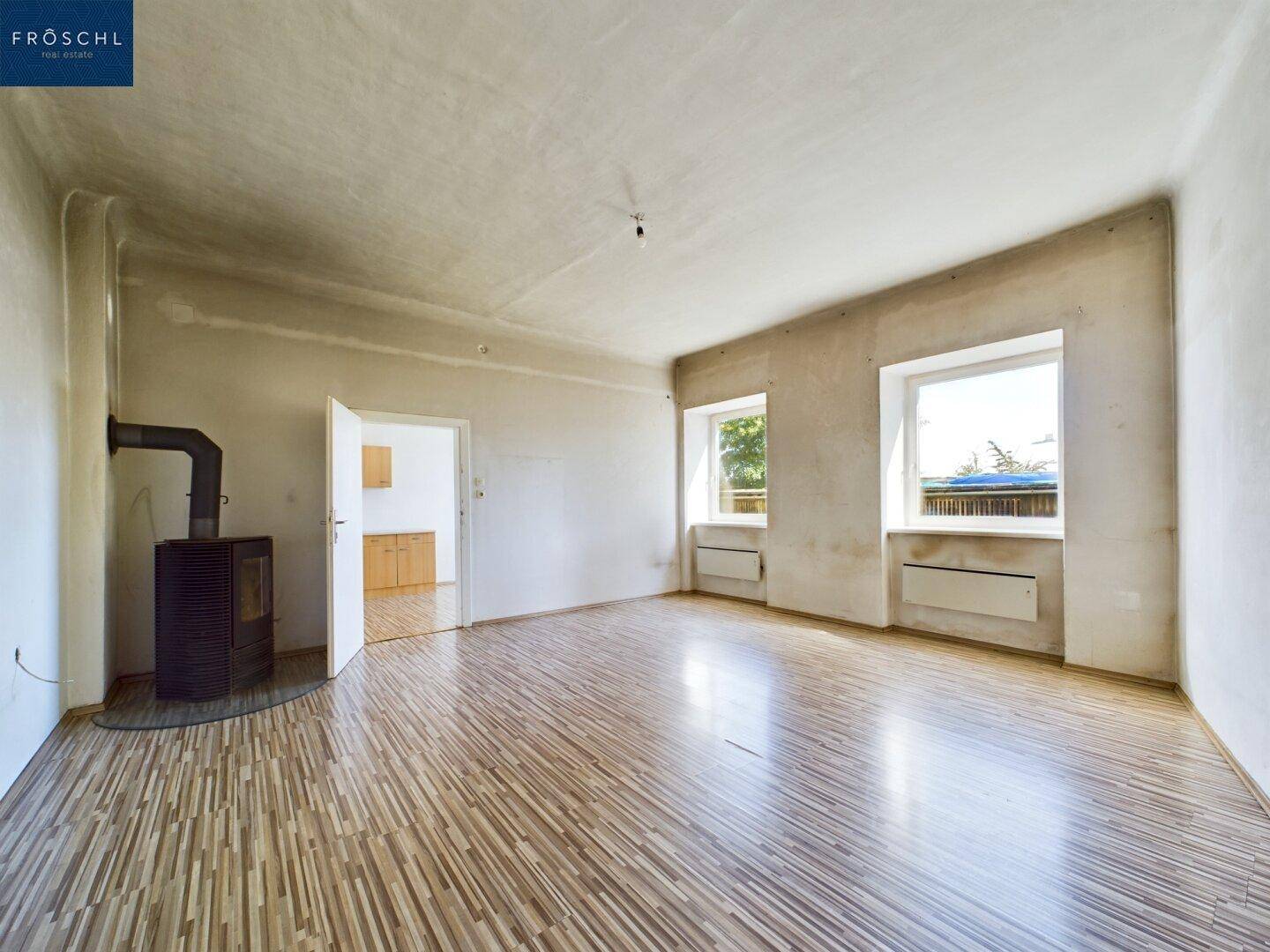 Geräumiger Wohnraum mit Holzboden, zwei Fenstern und einem modernen Kaminofen.
