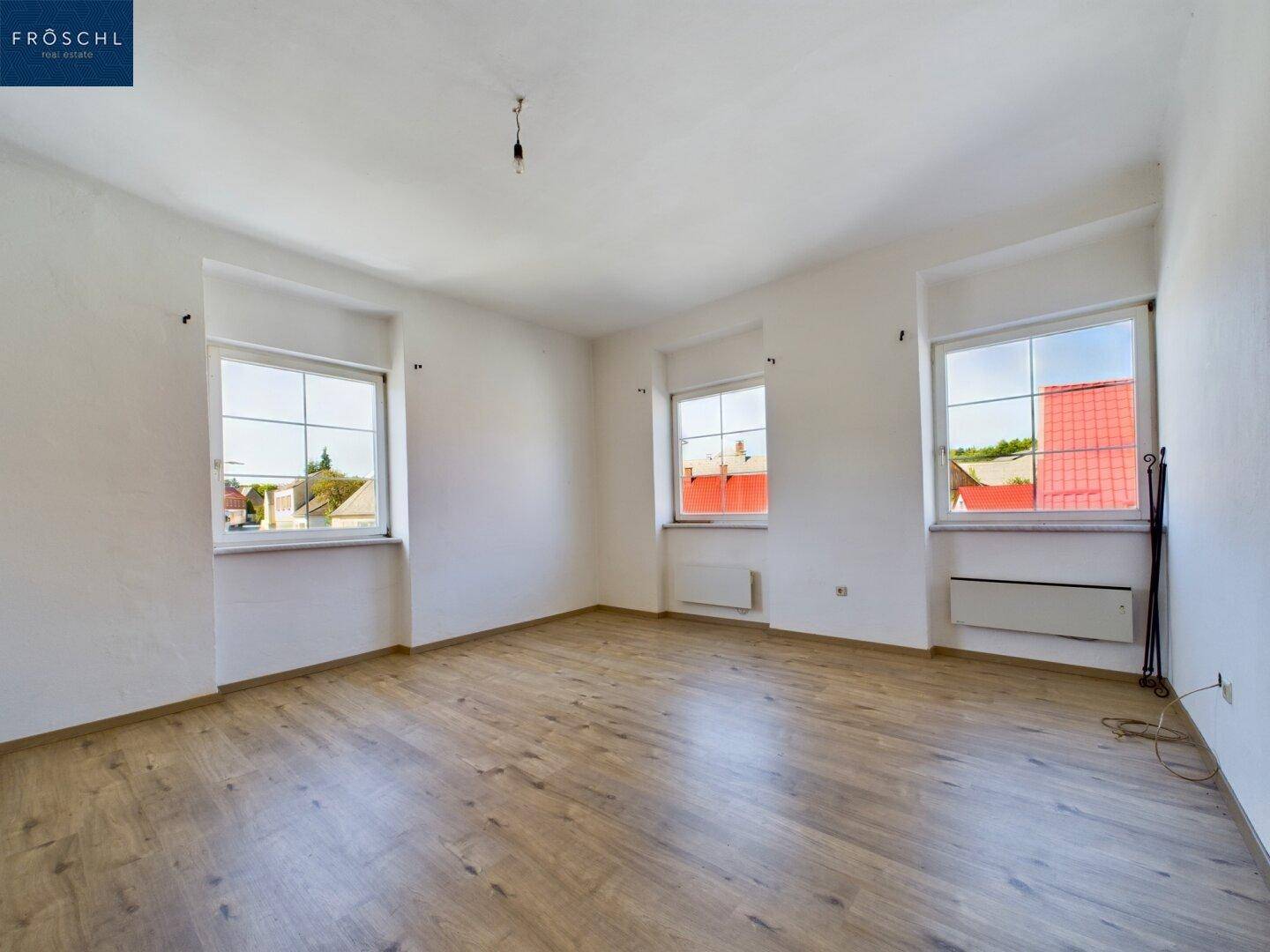 Heller Raum mit Holzboden, drei Fenstern und viel natürlichem Licht.