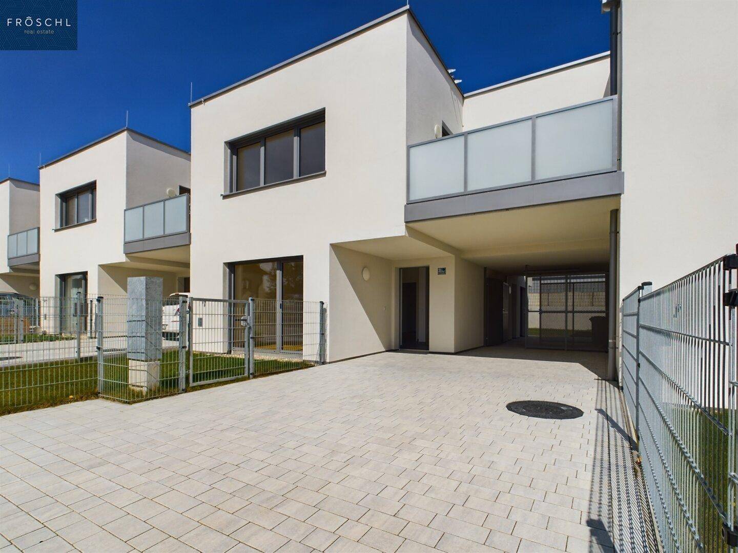 Moderne Reihenhäuser mit weißer Fassade, Balkonen und gepflasterten Parkflächen im Freien.