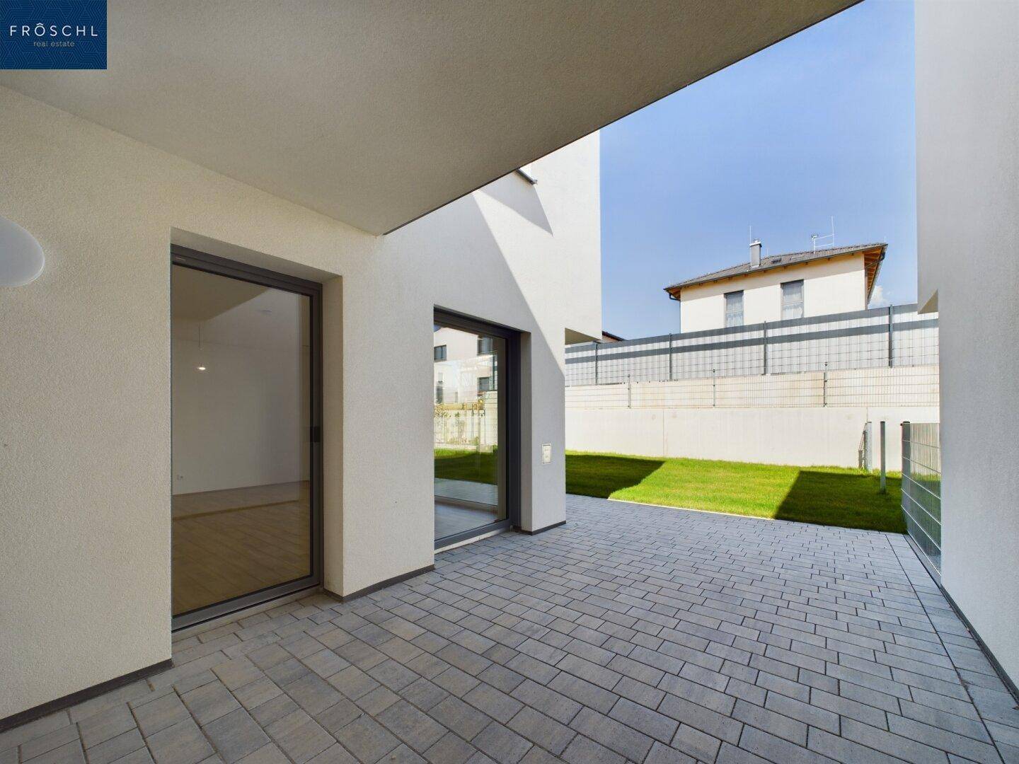Überdachte Terrasse mit grauen Pflastersteinen und Zugang zum Garten, ideal für entspannte Stunden im Freien.