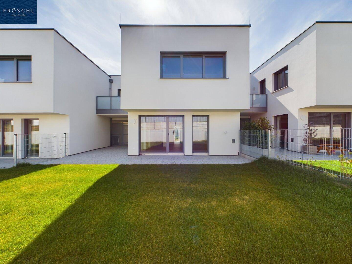Rückansicht der modernen Reihenhäuser mit großem Rasenbereich und gepflasterter Terrasse.