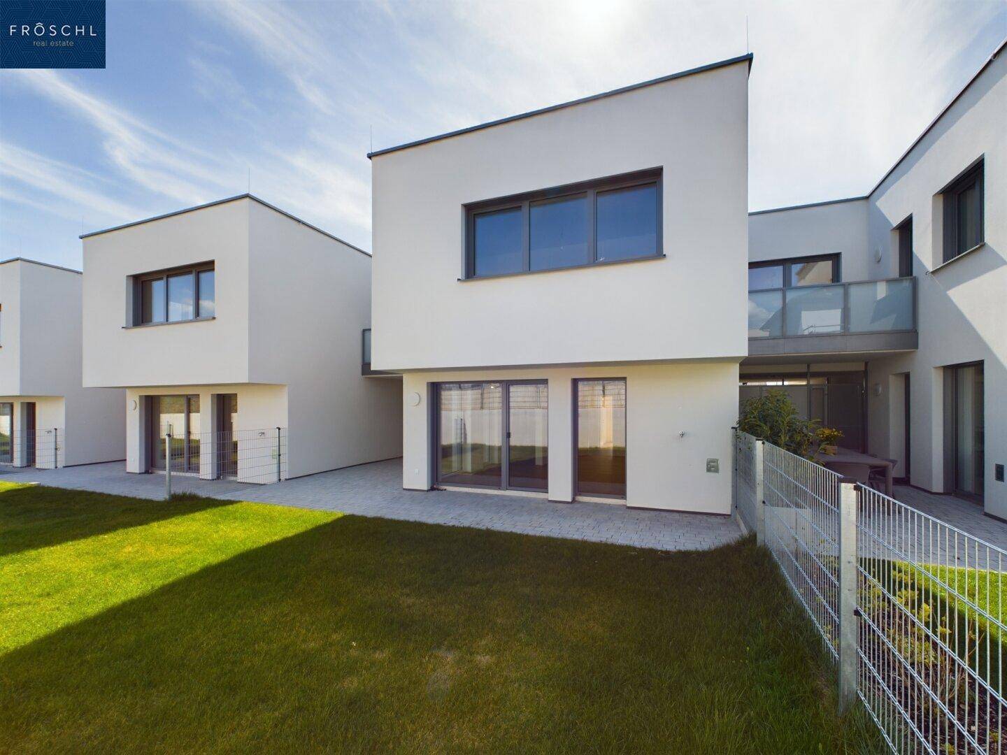 Seitenansicht der modernen Reihenhäuser mit gepflegtem Rasen und Zugang zur Terrasse.
