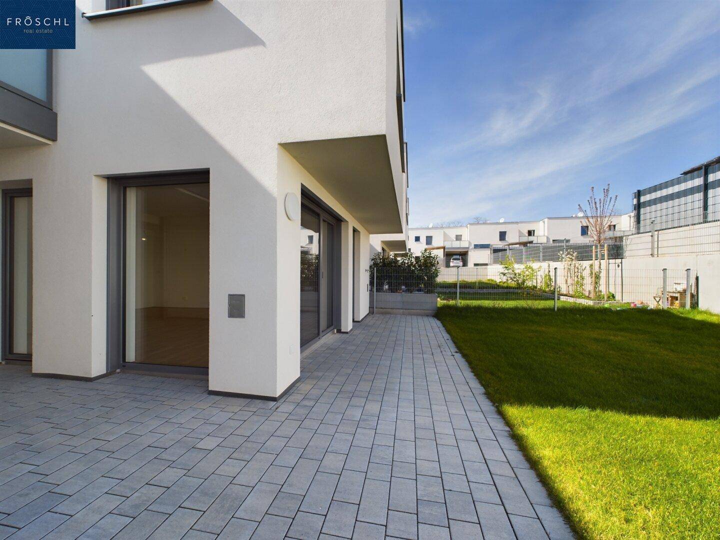 Seitlicher Blick auf die Reihenhäuser mit gepflastertem Weg, grünem Rasen und moderner Architektur.