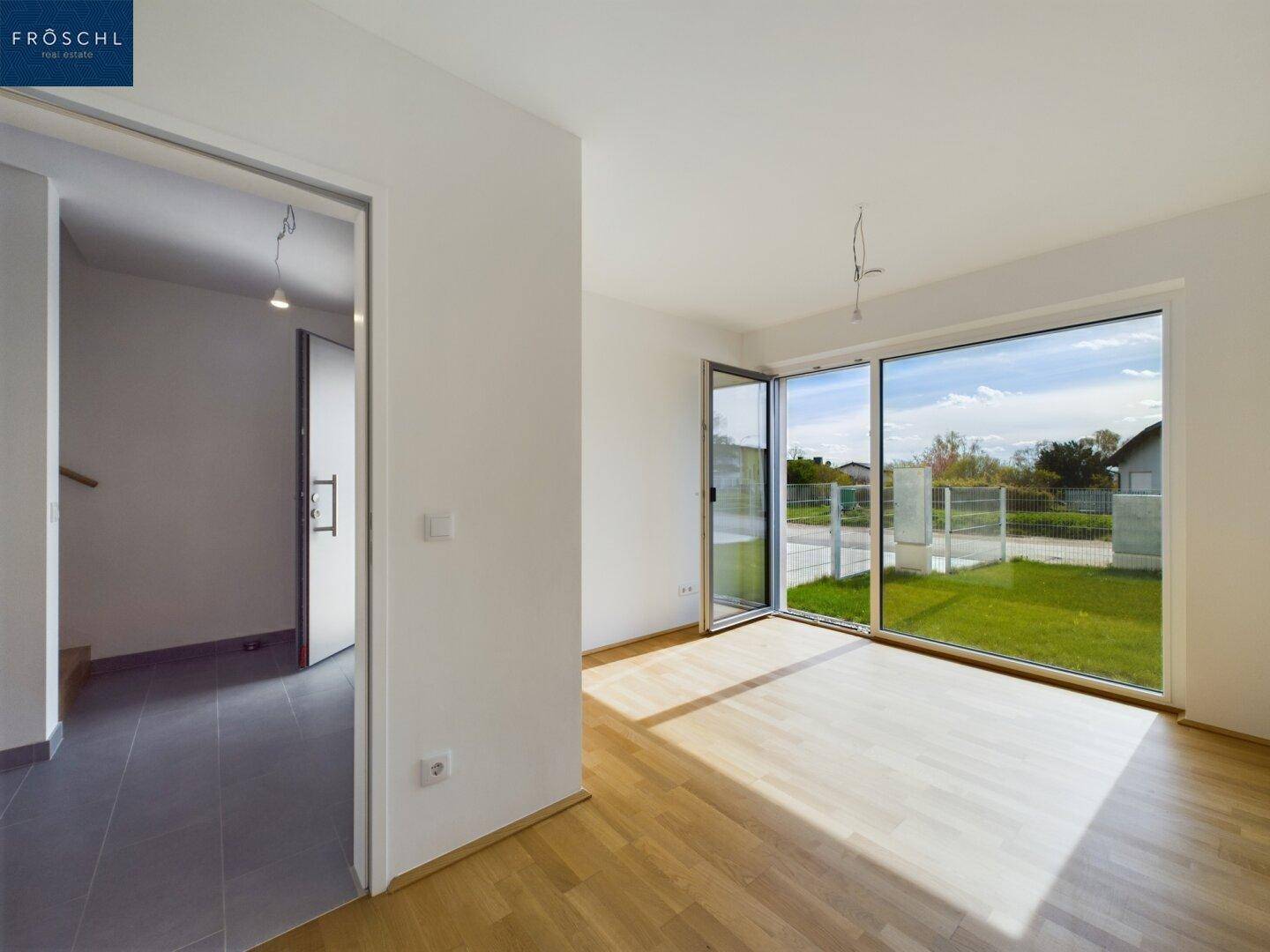 Helles Wohnzimmer mit Parkettboden und großen Fenstern, die viel Tageslicht hereinlassen.