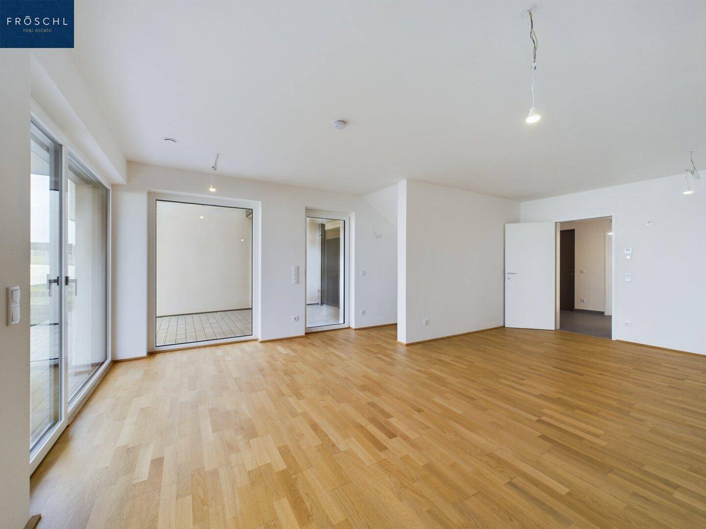 Geräumiges Wohnzimmer mit hellem Parkettboden und Zugang zu mehreren Bereichen des Hauses.