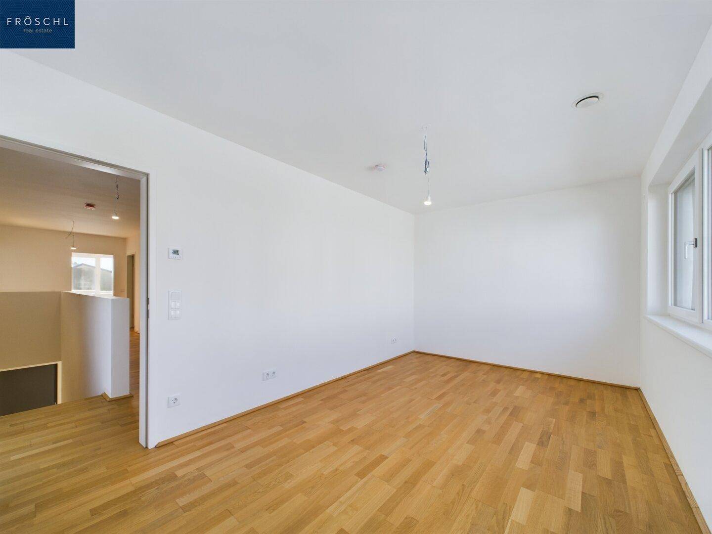 Helles Schlafzimmer mit Parkettboden und Fenster, das einen weiten Blick ermöglicht.