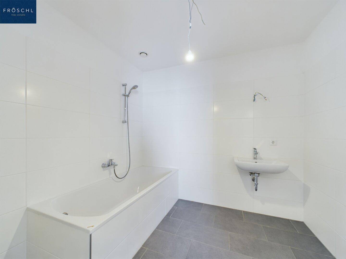 Modernes Badezimmer mit weißen Fliesen, Badewanne und Waschbecken, in neuwertigem Zustand.