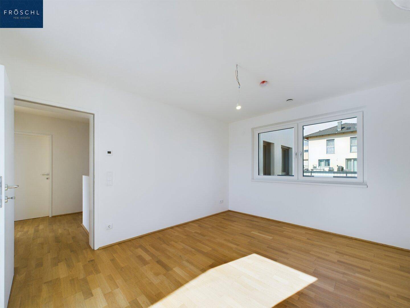 Geräumiges Schlafzimmer mit Parkettboden und Fenster, das einen Blick auf die Umgebung bietet.