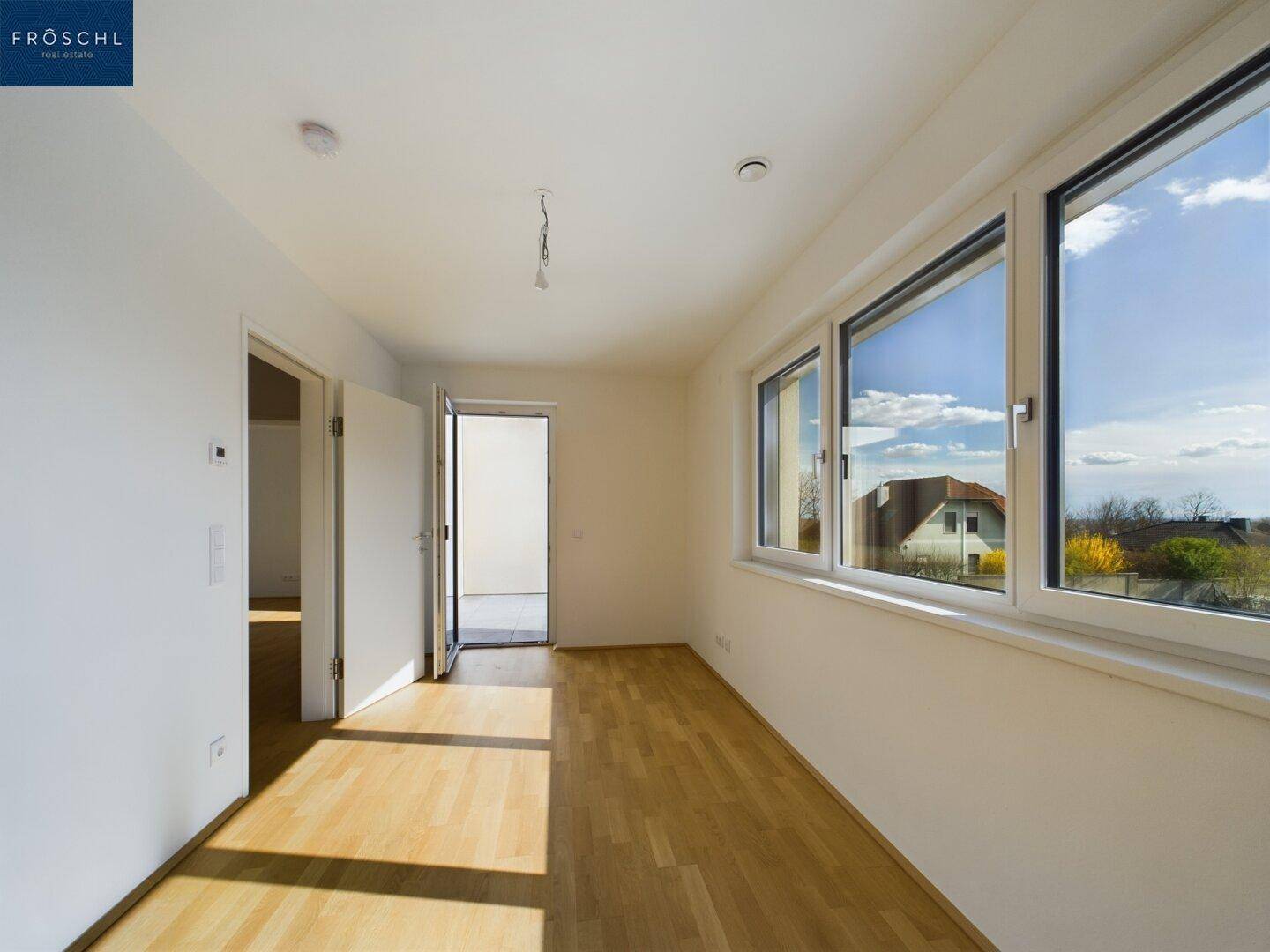 Helles Schlafzimmer mit Parkettboden und großen Fenstern, die viel Tageslicht hereinlassen.