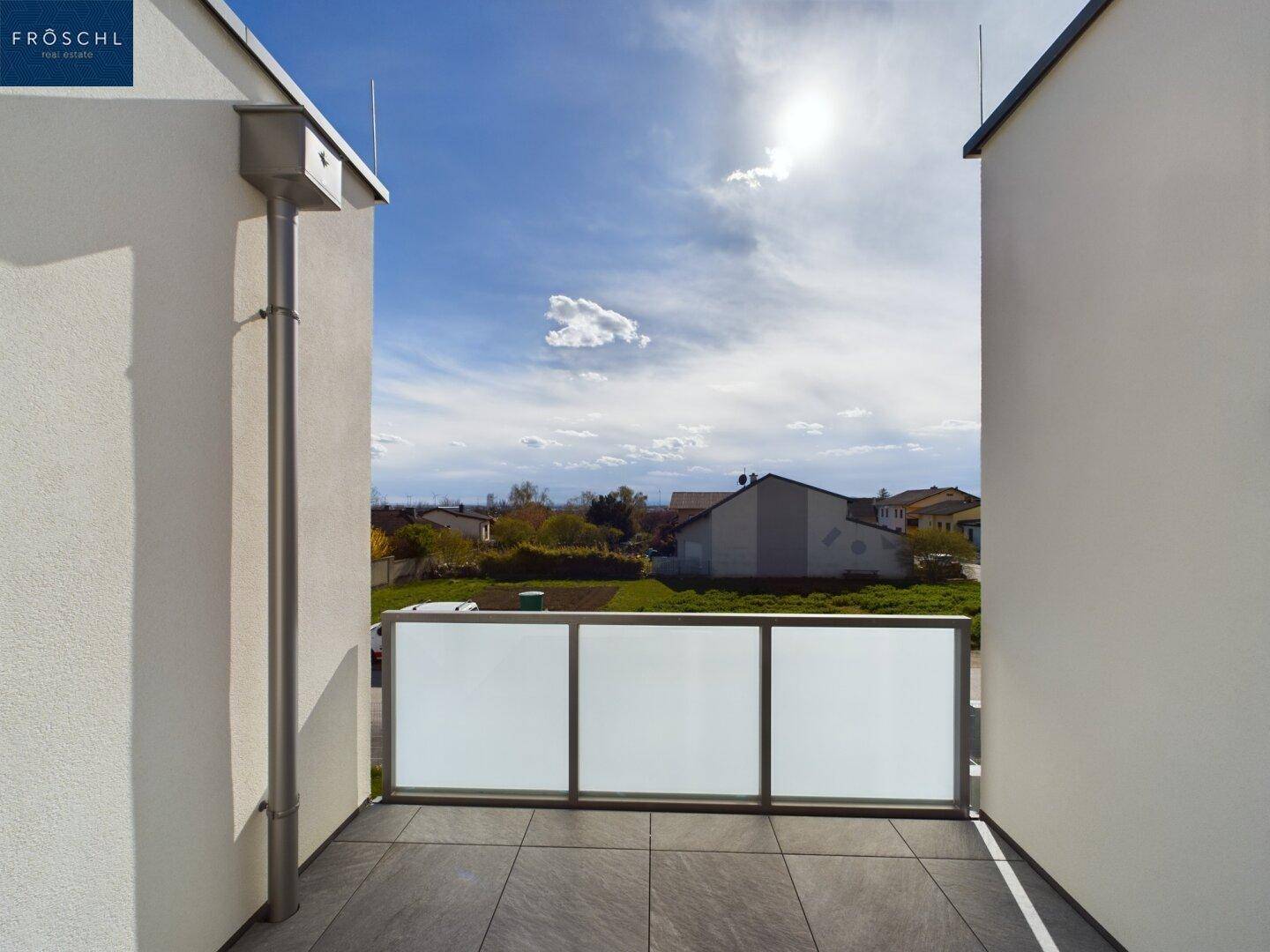 Sonniger Balkon mit Fliesenboden und Blick auf die umliegende Landschaft unter blauem Himmel.