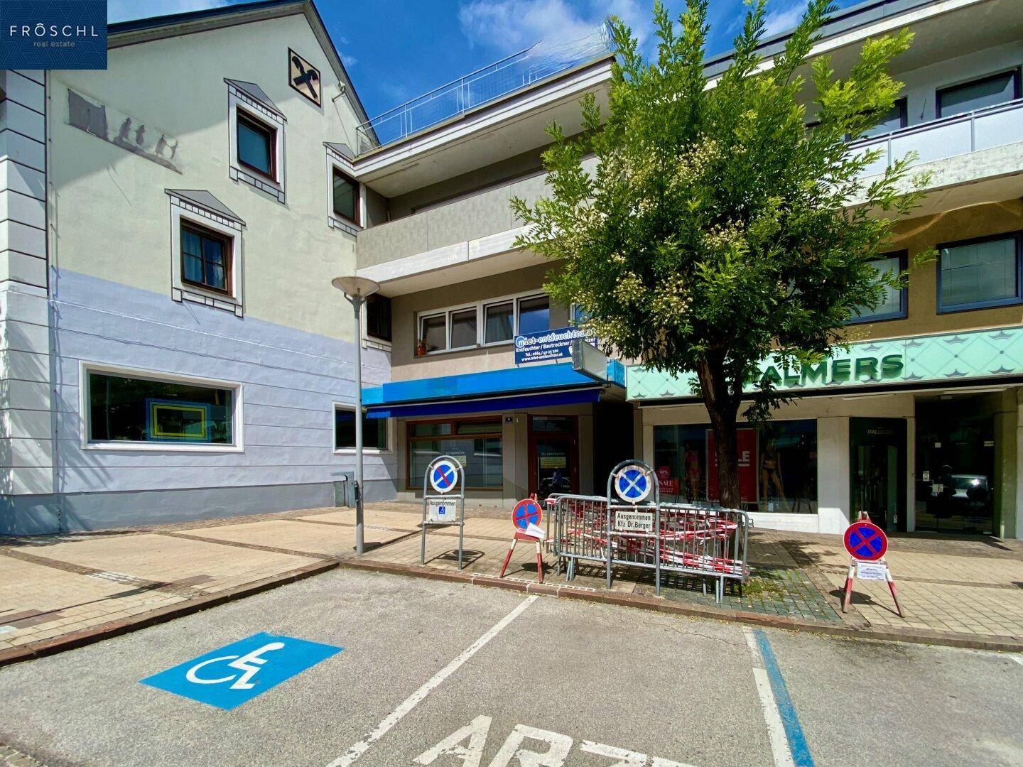 Geschäftsgebäude mit Schaufenstern und einem Behindertenparkplatz in der Vorderansicht.