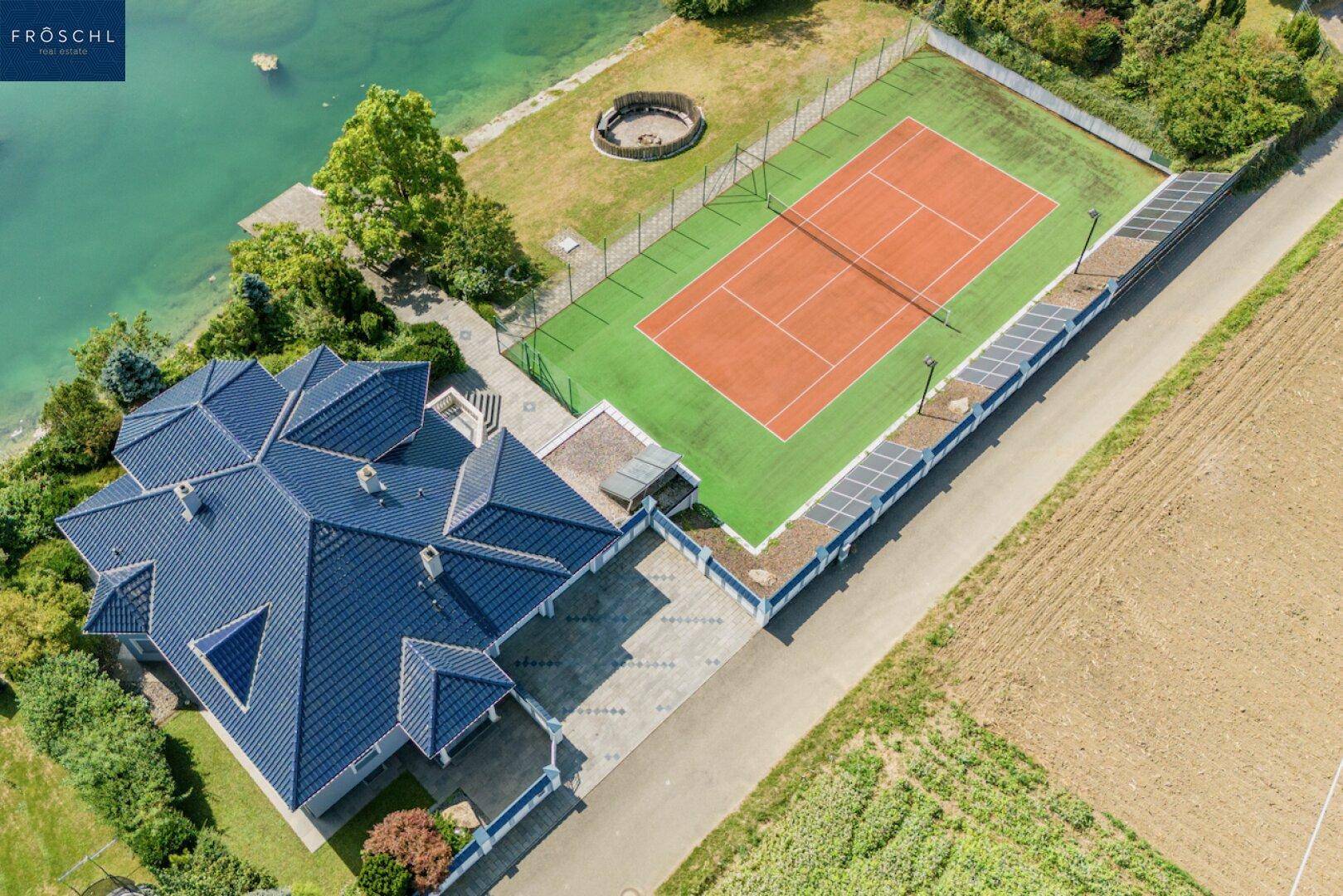 Draufsicht auf das Anwesen mit Haus, Tennisplatz und direktem Seezugang.