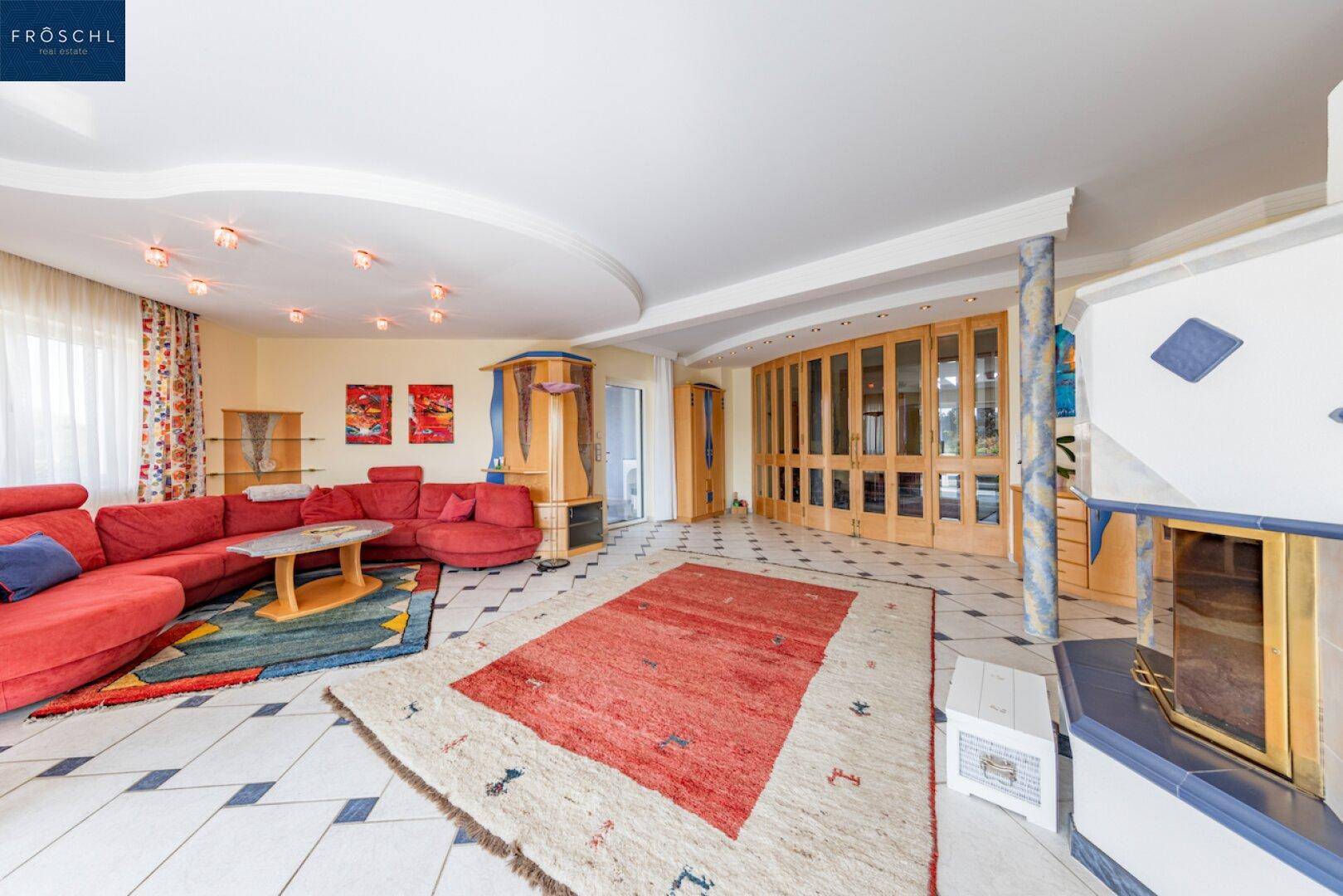 Gemütliches Wohnzimmer mit rotem Sofa, Kachelofen und dekorativen Fliesenböden.