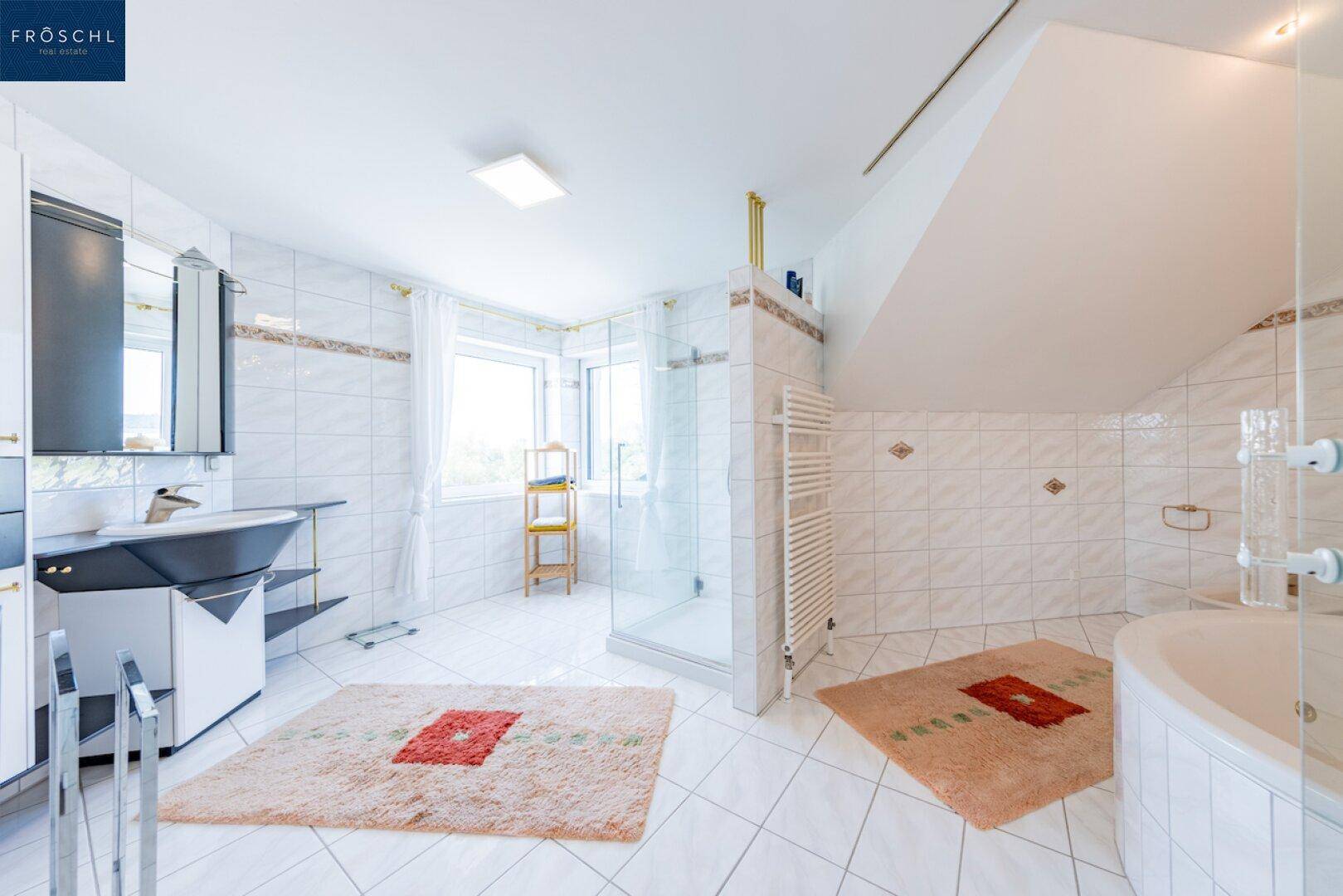 Geräumiges Badezimmer mit weißen Fliesen, Dusche und Eckbadewanne unter Dachschräge.