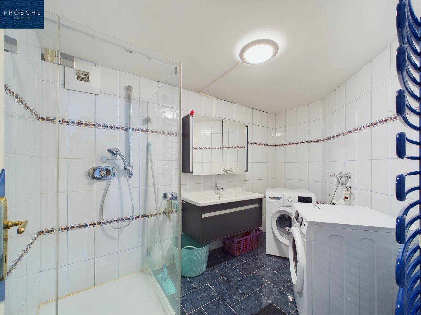 Praktisches Badezimmer mit Dusche, Waschbecken und integrierten Waschmaschinen.
