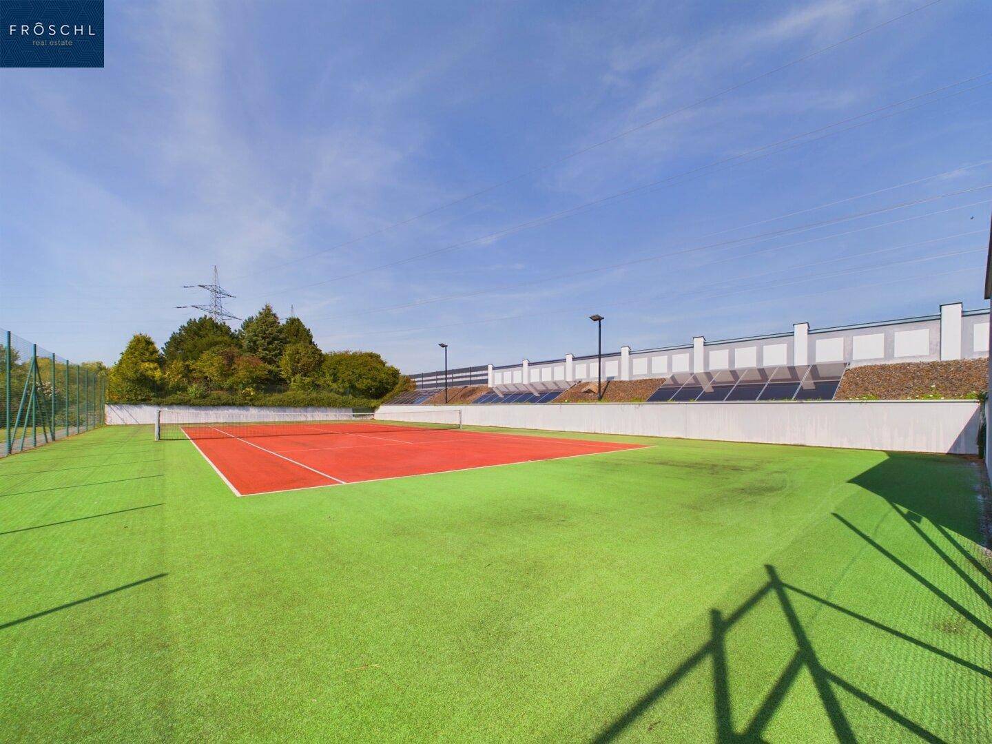 Gepflegter Tennisplatz mit Kunstrasen und Sandplatz, umgeben von einem Zaun.