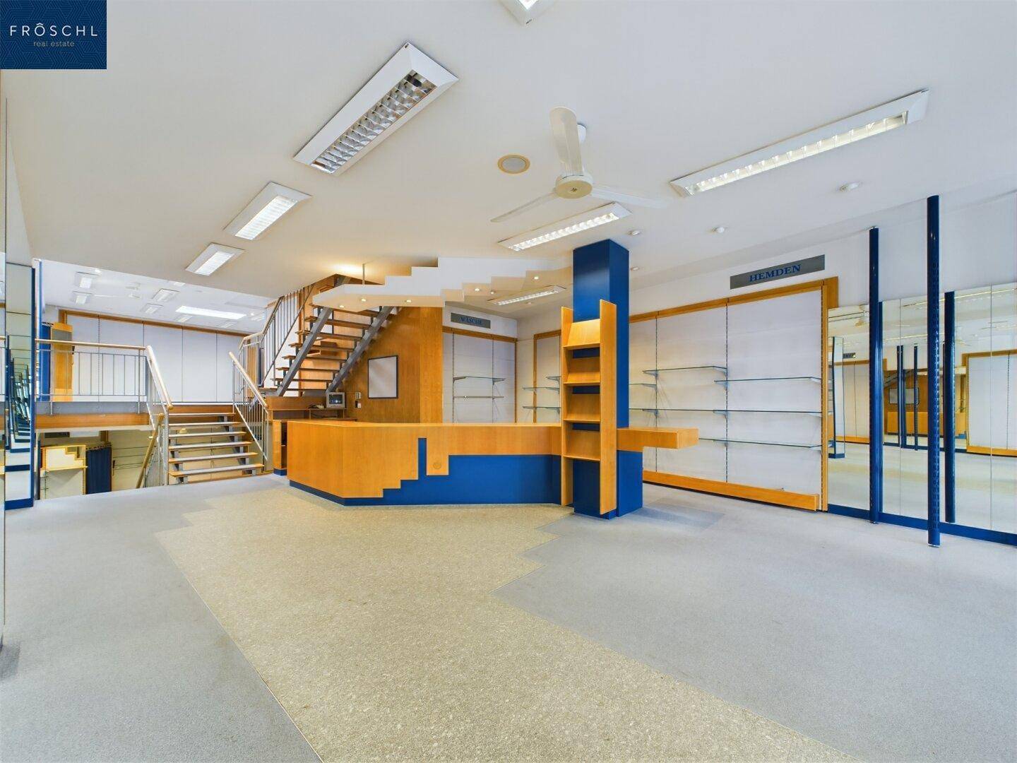 Der Empfangsbereich des Geschäfts mit einer markanten blauen Theke und einer offenen Treppe zum Obergeschoss.