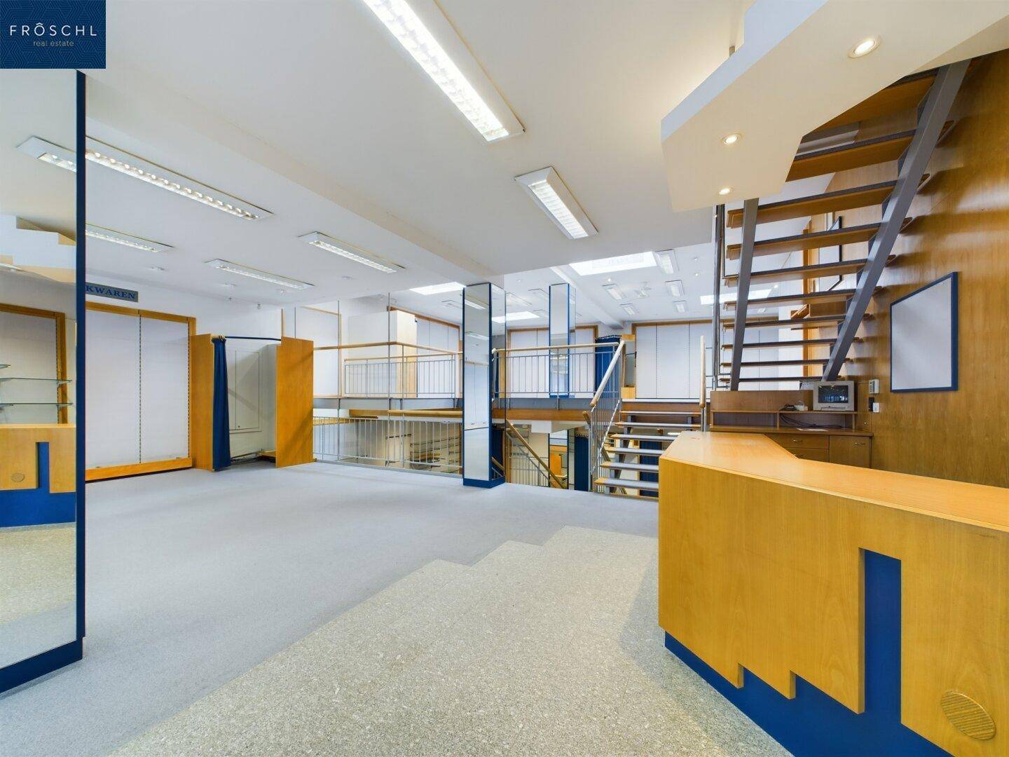Empfangsbereich im Verkaufsraum mit Holzelementen, einer Theke und einer offenen Treppe zu den oberen Etagen.