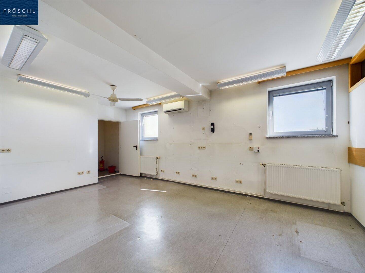 Leerer Raum mit Fenstern, Heizkörpern und einer Klimaanlage, ideal als Büro oder Lagerfläche.