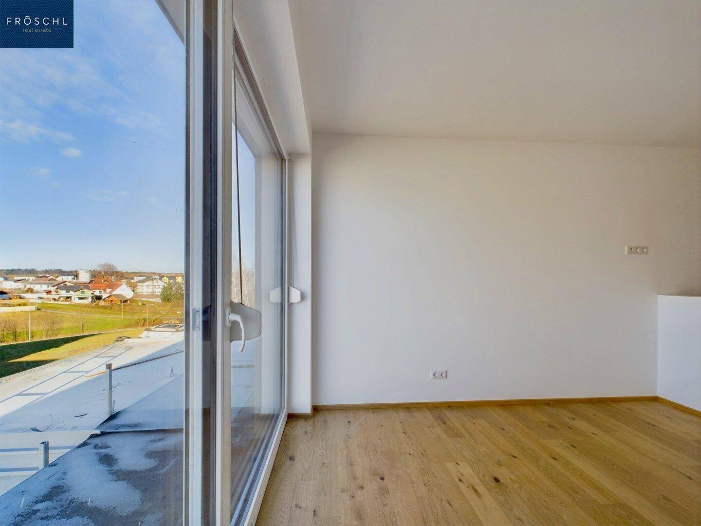 Heller Wohnraum mit Holzboden und bodentiefen Fenstern, die einen weiten Ausblick bieten.