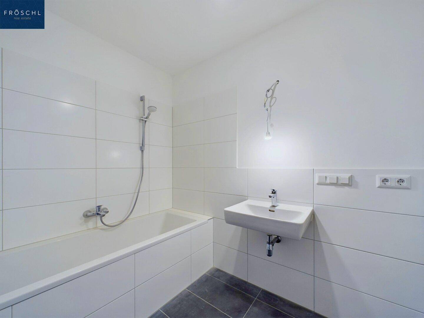 Modernes Badezimmer mit weißen Wandfliesen, dunklem Boden und Badewanne mit Duschfunktion.